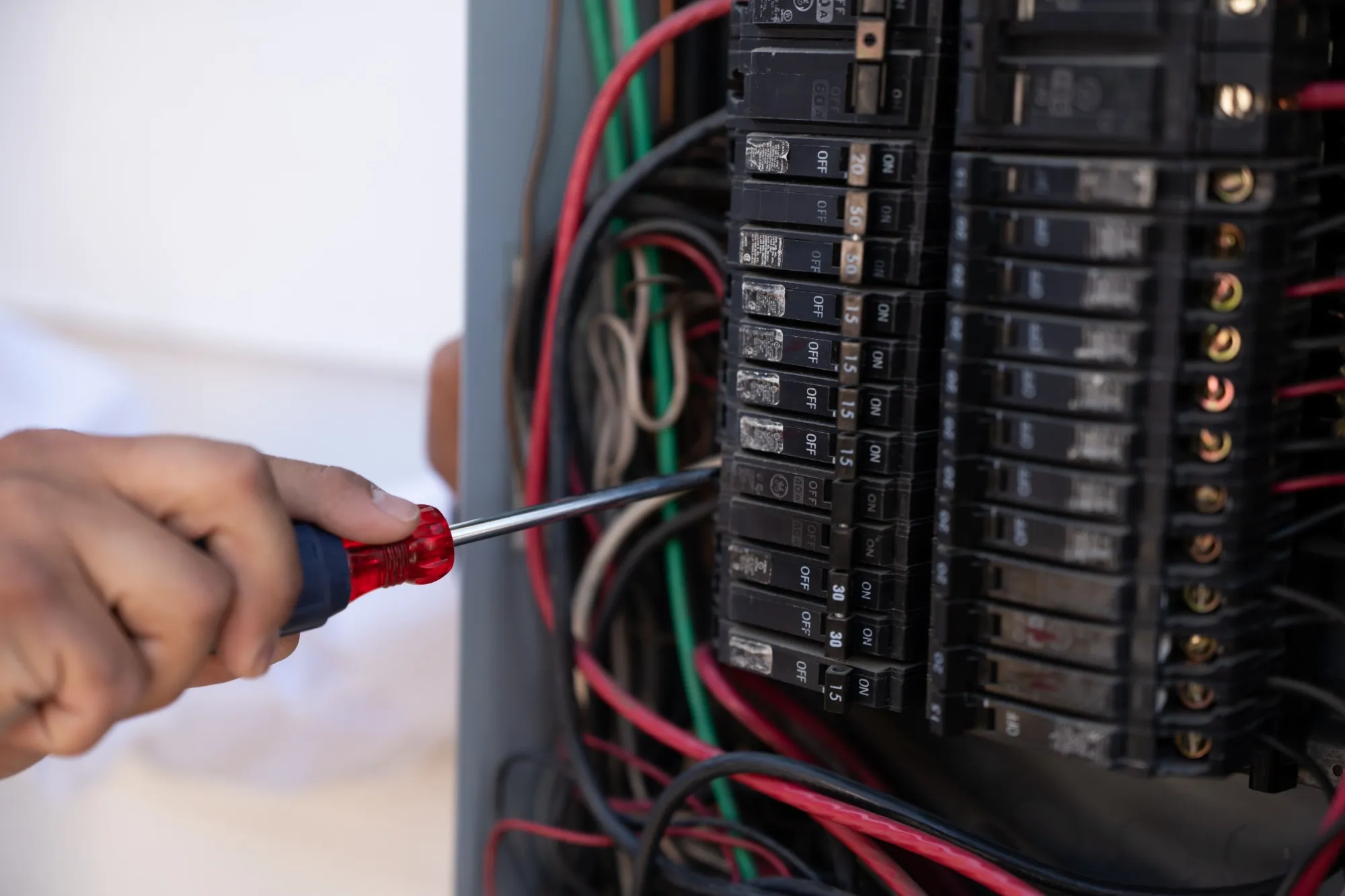 Electrician working inside an open electrical panel, tightening a breaker connection with a screwdriver